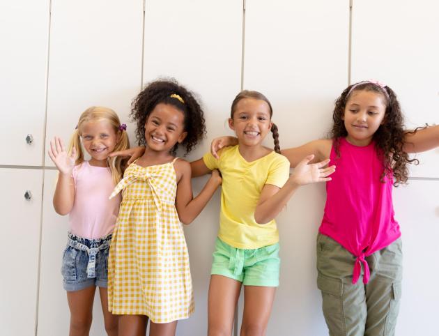 Portrait of cheerful cute multiracial elementary schoolgirls with arm around waiting while standing. unaltered, childhood, together, education, enjoyment and back to school concept.